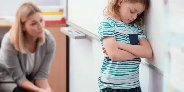 Offended child stands with his arms folded in the classroom, his back to the teacher